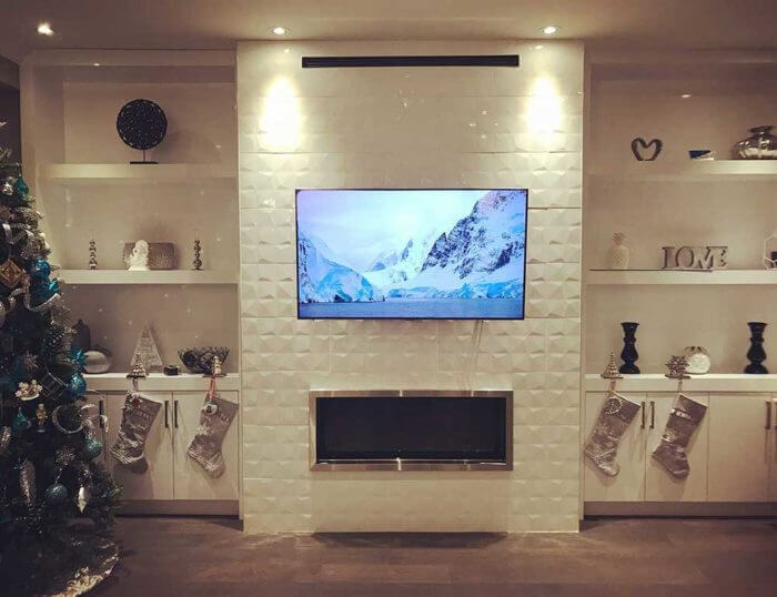 A flat-panel TV mounted flush above a tiled fireplace surround, centred between built-in shelving in a living room