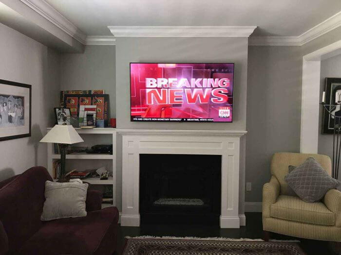A television mounted above a fireplace in a living room, the kind of install where a large panel and a masonry wall usually mean calling a professional