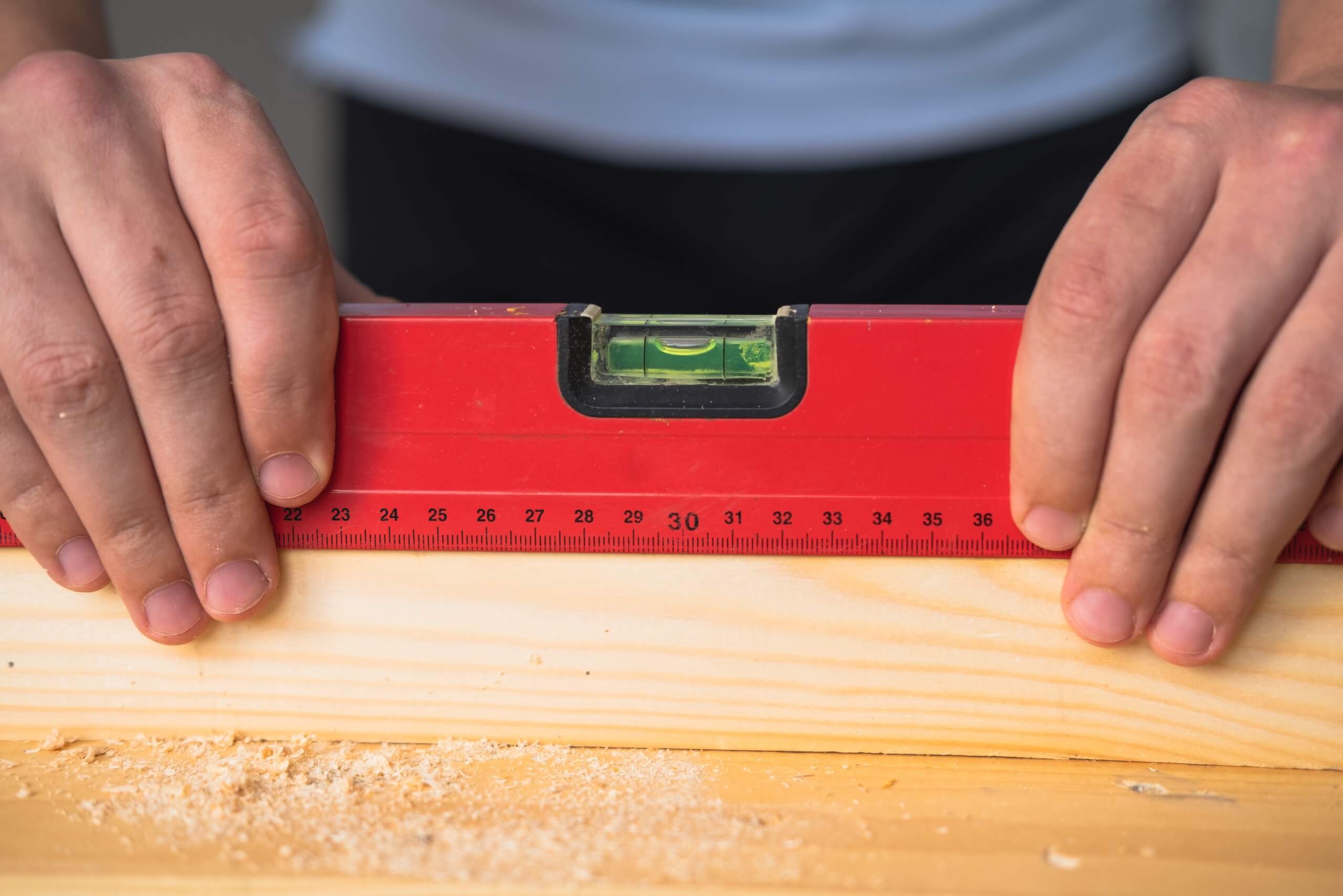A spirit level being held across timber, the tool that decides whether a TV wall plate goes on straight