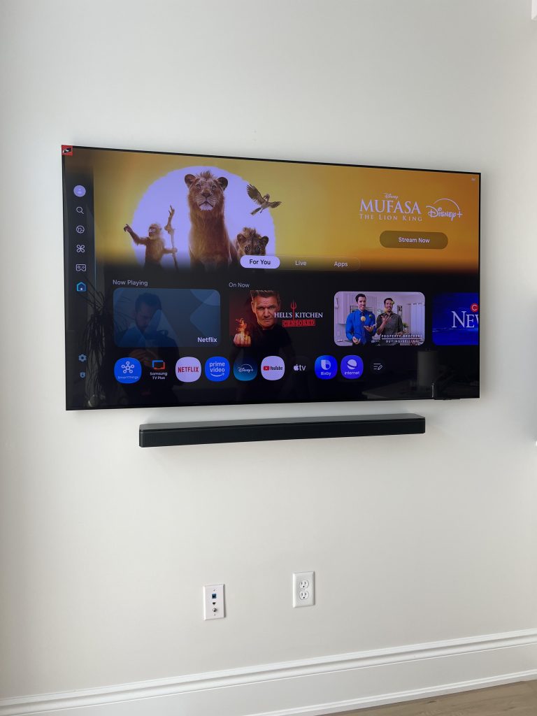 Wall mounted TV and soundbar with no visible cables and a recessed outlet plate below