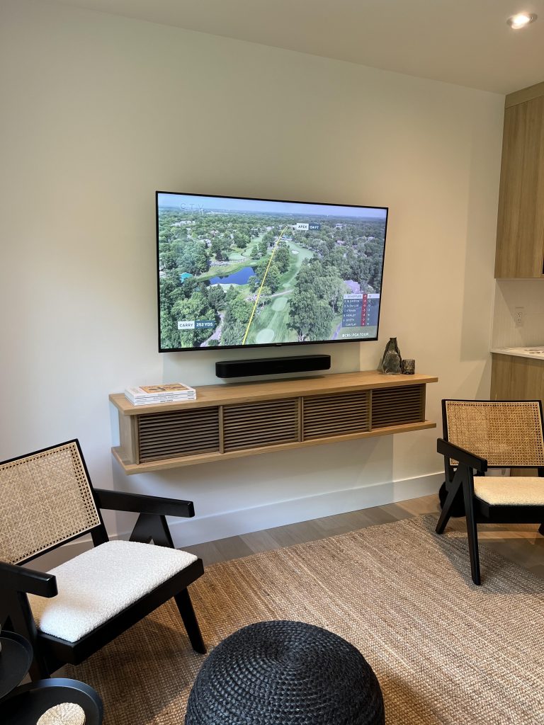 Soundbar resting on a floating wooden shelf beneath a wall mounted TV