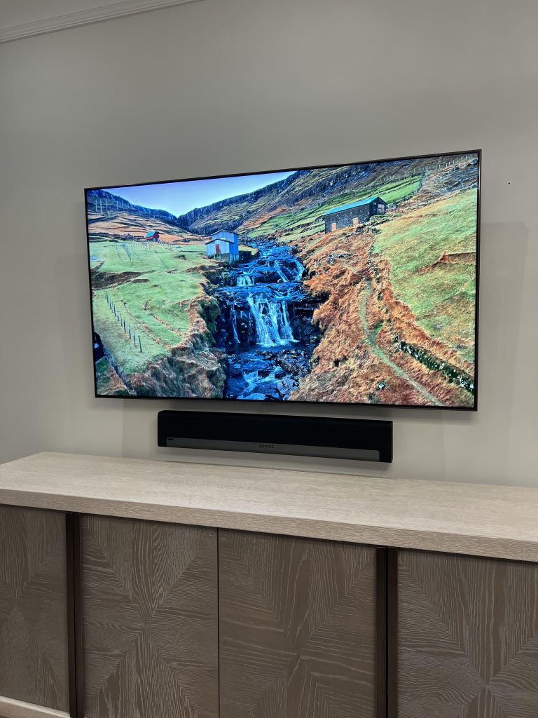 Soundbar wall mounted directly below a large TV above a low cabinet